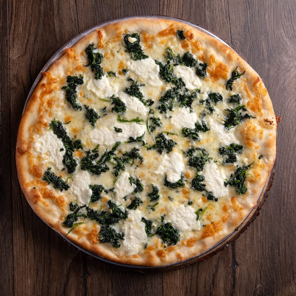 A whole New York-style white pizza with spinach and ricotta cheese on a wooden table.