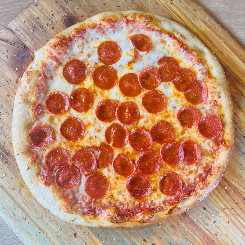 A whole New York-style pepperoni pizza with melted cheese and red sauce on a wooden board.