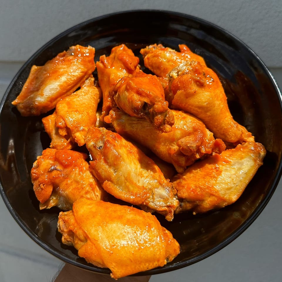 A black bowl filled with golden-brown chicken wings coated in a vibrant orange sauce.