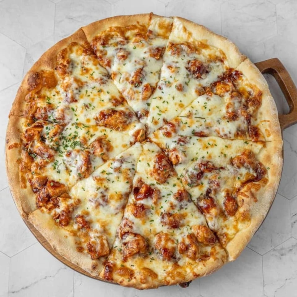 A whole New York-style pizza with melted cheese, chicken, and parsley on a wooden paddle.
